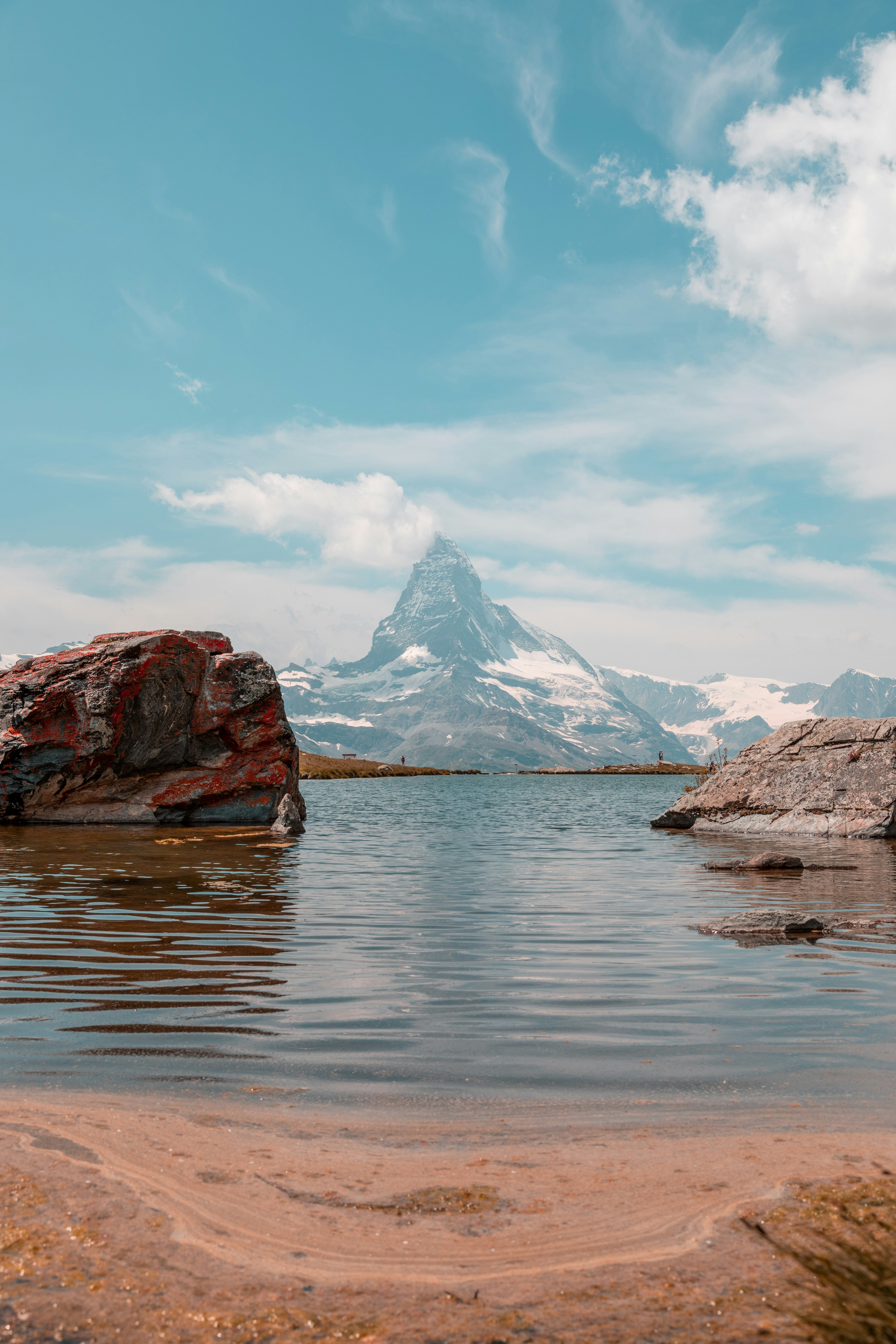 brown and white mountains near body of water under blue sky during daytime